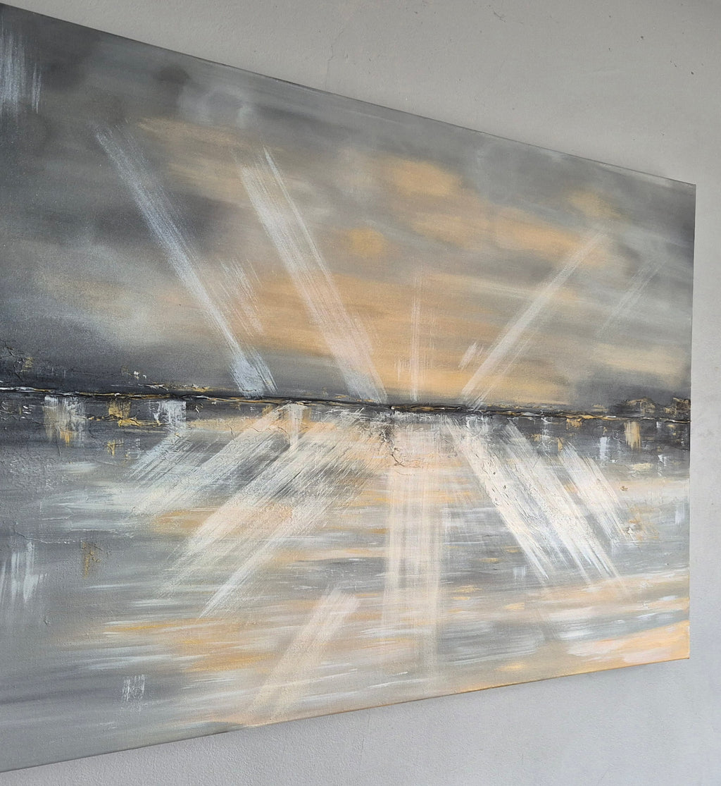 An abstract landscape painting on canvas, featuring radiating white brushstrokes over a gray and black background with warm beige and gold tones near the horizon, displayed on a light gray wall.