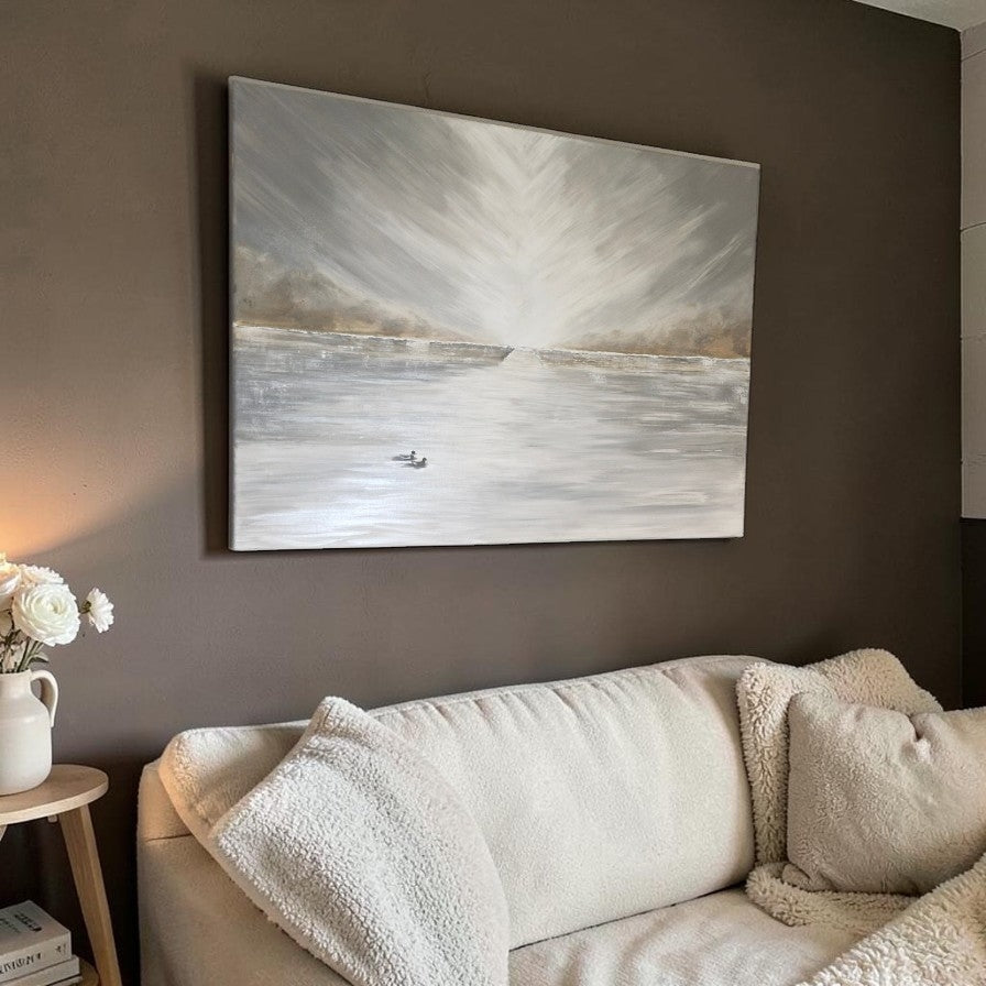 A large square canvas painting of a snowy or icy lake scene with a small boat, displayed on a dark brown wall above a cream-colored sofa in a living room setting.